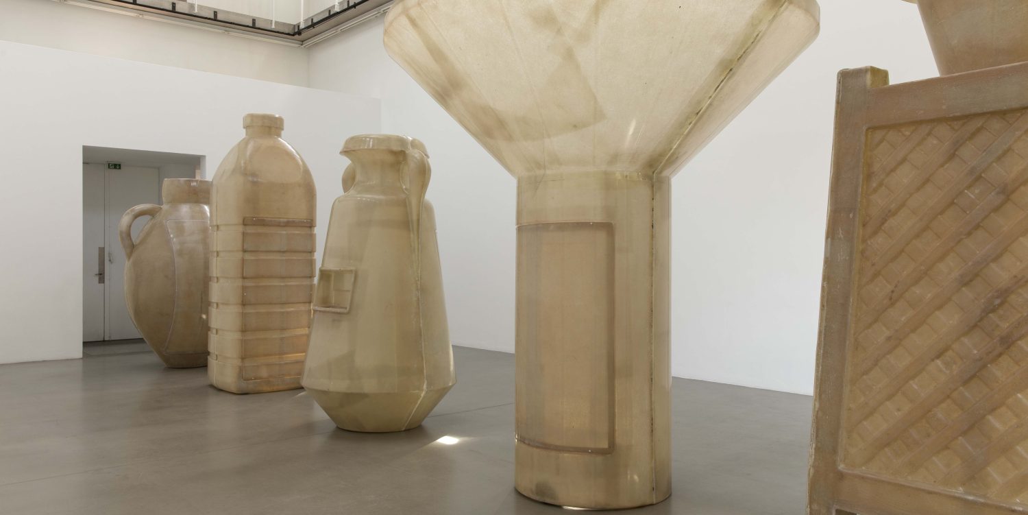Five large fibreglass water vessel sculptures stood in a row in a large bright exhibition space.