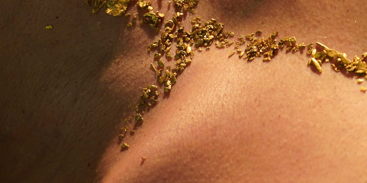 A close-up image of small pieces of gold laying on a person’s neck and upper chest.