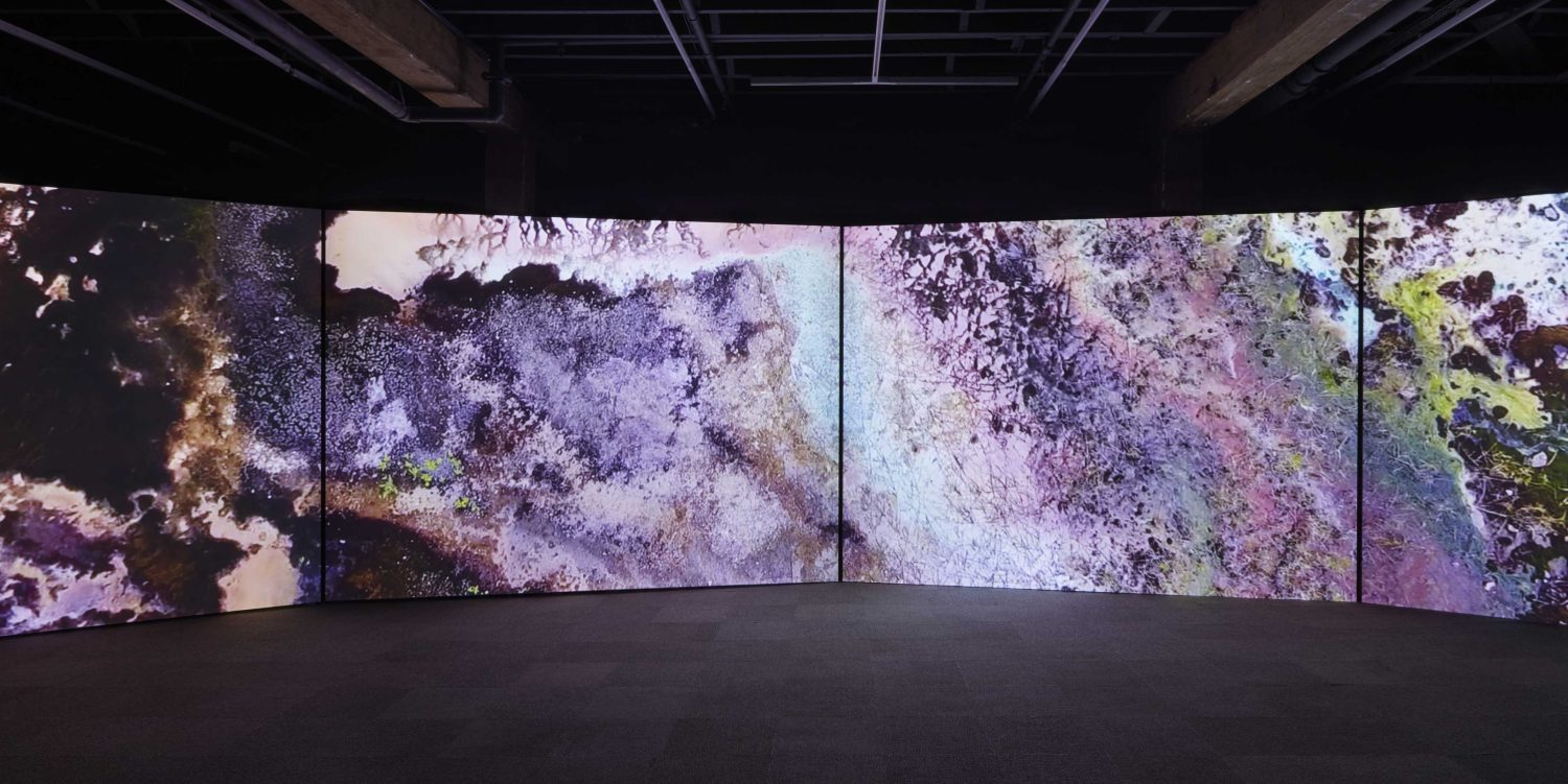 An installation of HD video on four screens showing an arial view of the topography of the mined landscape of the Autonomous Region of Bougainville.