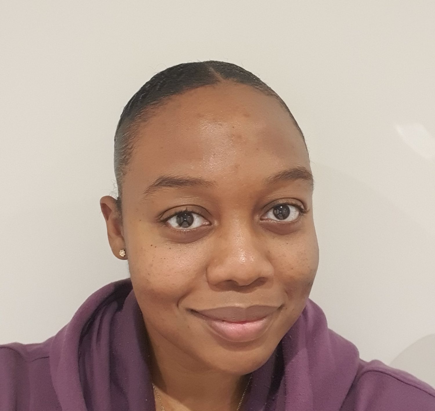 A headshot of a woman called Beloved Elizabeth Adonai looking and smiling directly at the camera. She is wearing a purple hoody and there is a white background behind her.