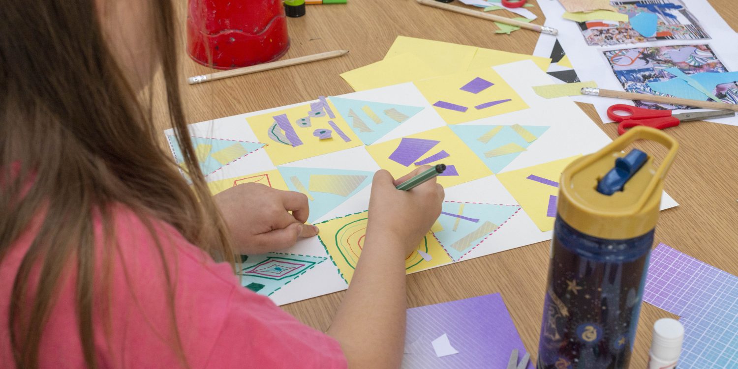 A child taking part in a creative activity at Mostyn. Llandudno. Credit: Mostyn A girl with long hair is using a pen to do some drawing. Around her are craft materials such as scissors, glue, pens and card