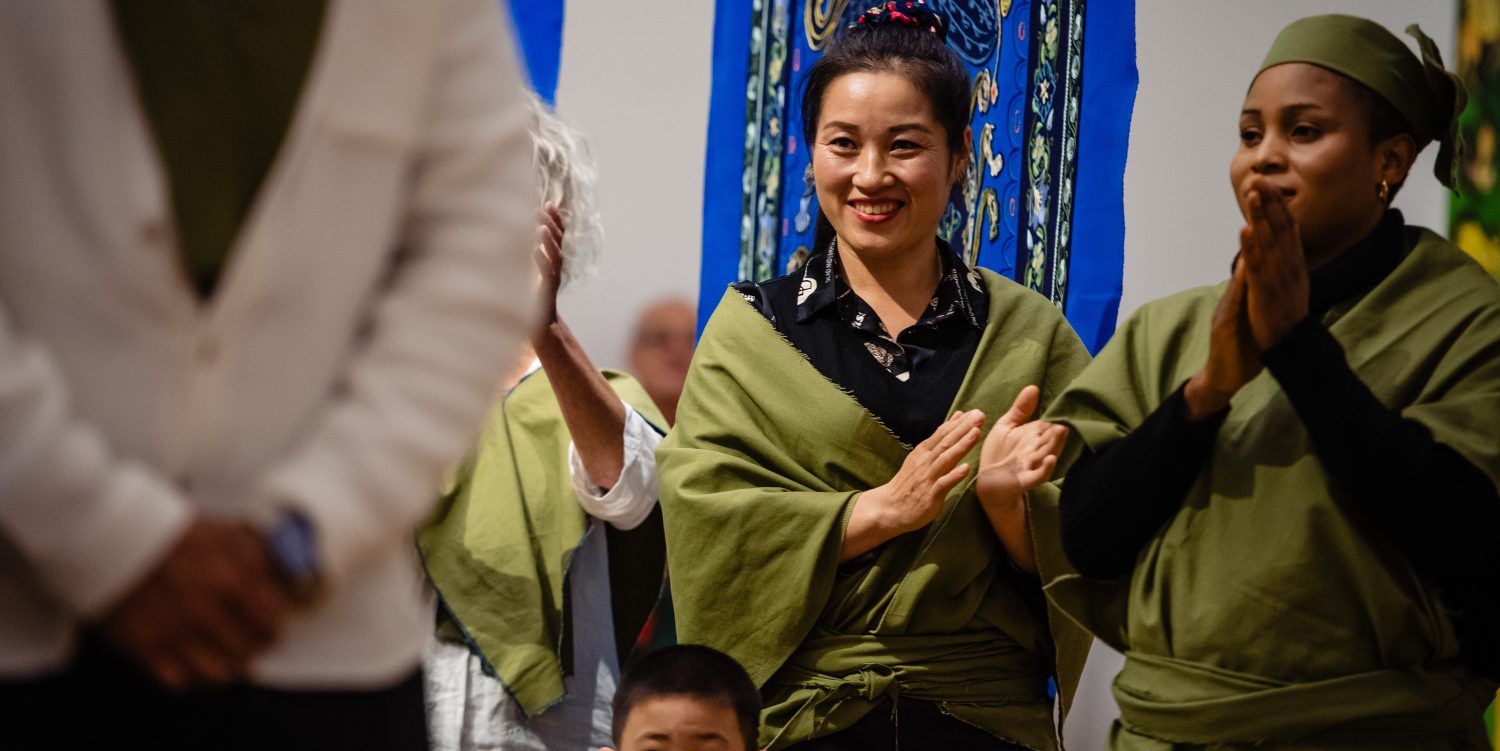 Two women wearing khaki clothes are smiling and clapping. There is a young boy stood in front of them.