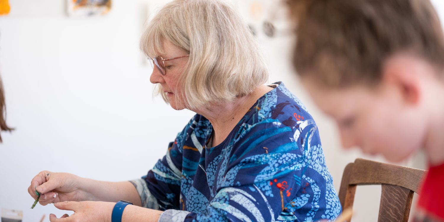 A woman wearing a blue top and glasses is using fern for printing. A person in the foreground is out of focus.