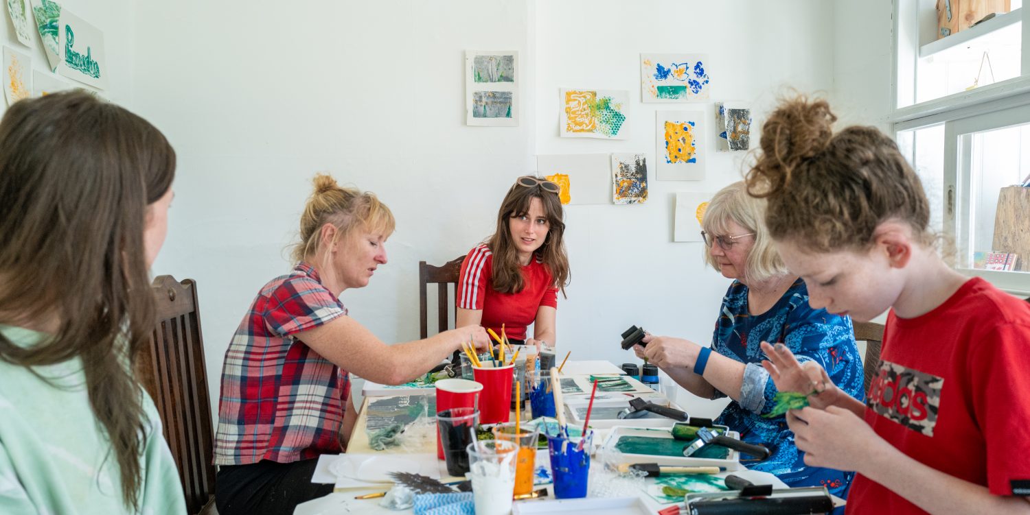 A group of women are sat around a table monoprinting.