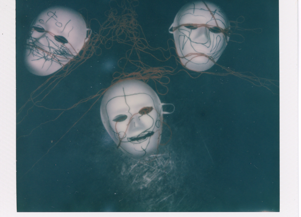 A polaroid of three white masks with string placed over them.