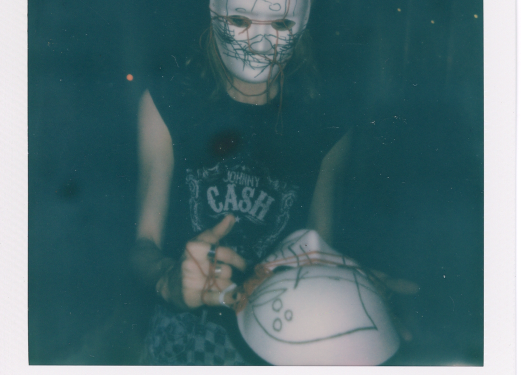 A polaroid of a person wearing a white mask. They're also holding a white mask.